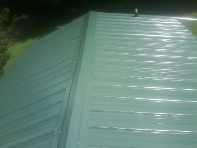 New green metal panels meeting at the ridge of a roof — Flat Roof Repair work by our crew in Grand Rapids