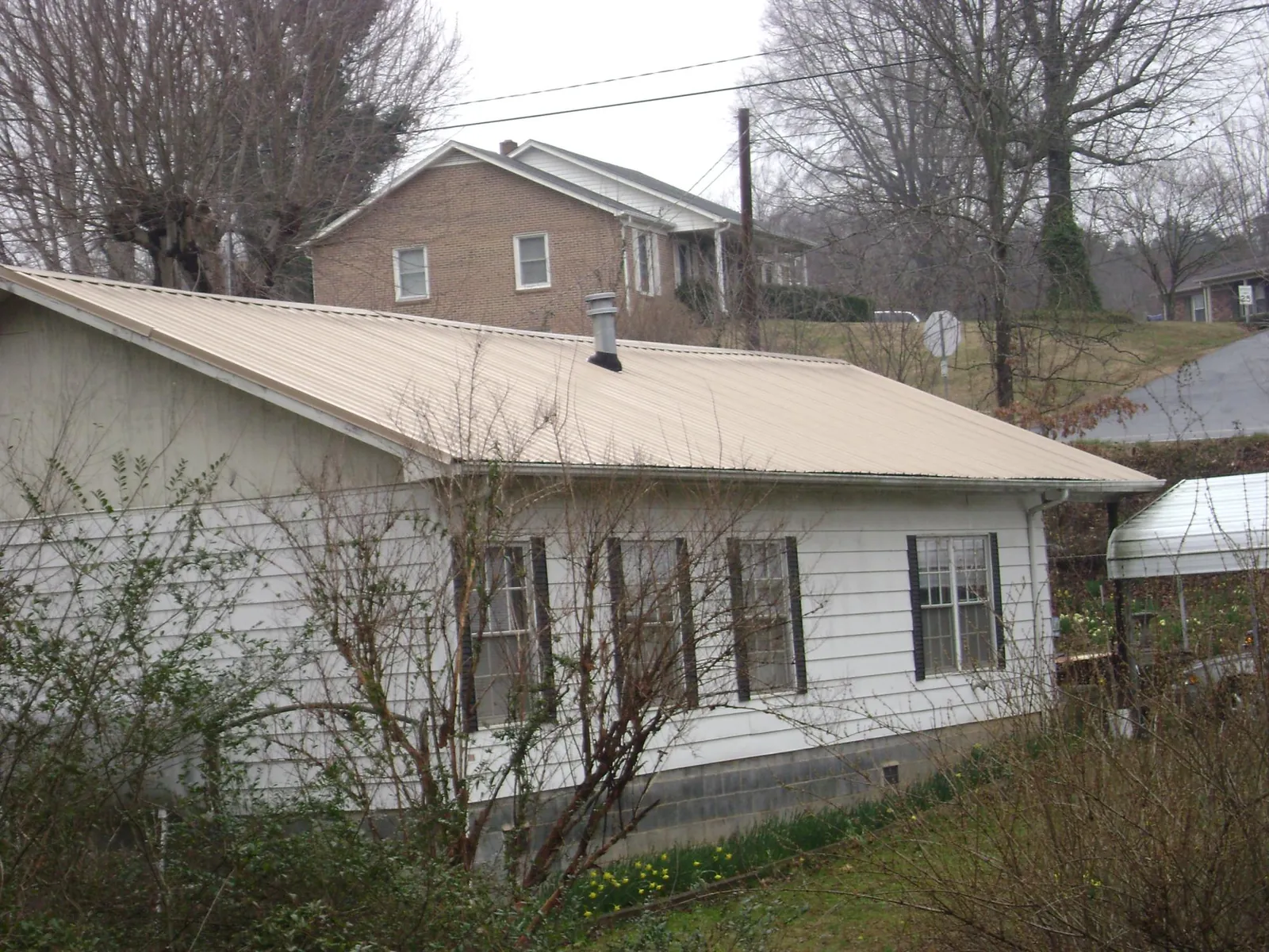 Tan metal roof on a white sided house set into a hillside — Commercial Roofing by Roofing Brothers in Grand Rapids